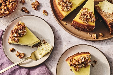 Carrot Cake Cheesecake on a table with slices on plates showing a golden cheesecake rimmed with nuts. - select to zoom