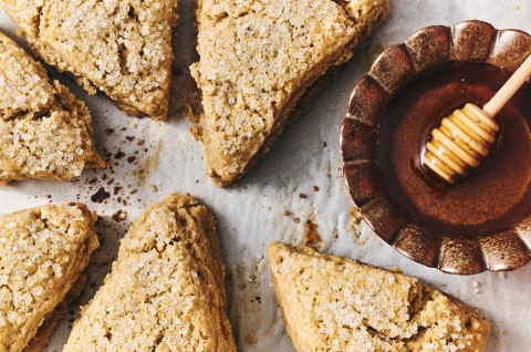 Looking down on Golden Wheat Scones with coarse sugar on top of them and a bowl of honey with a wooden honey wand. - select to zoom