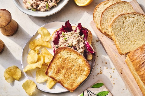 A sandwich, made with King Arthur's Classic Sandwich Bread, on a plate with chips and slices of bread on the table. - select to zoom