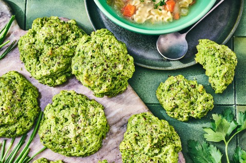Green Goddess Herb Biscuits on cutting board with a bowl of soup in the frame. - select to zoom