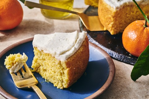 A slice of whole orange cake ona. blue plate with a bite on a fork. - select to zoom