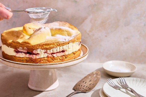 Karpatka Cake on a cake stand being dusted with powdered sugar. - select to zoom