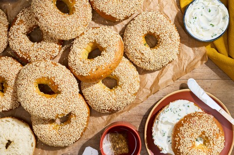 Sesame Sourdough Discard Bagels arranged on parchment with a shmear of cream cheese and a sliced bagel on a plate. - select to zoom