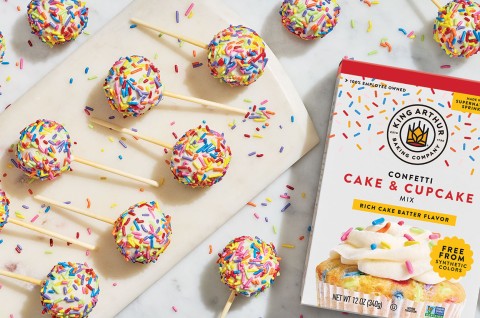 Confetti Cake Pops on a countertop with a box of confetti cake and cupcake mix made by King Arthur Baking in the frame. Seen from above. - select to zoom