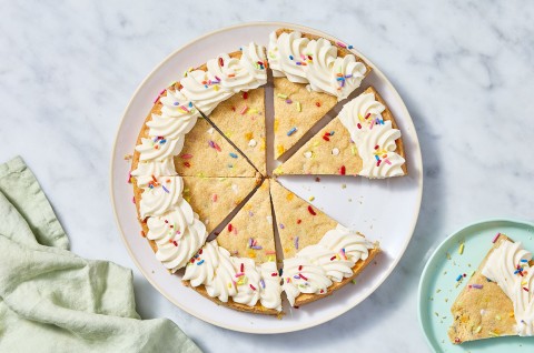 Sliced Confetti Sugar Cookie Cake on a marble countertop with a piece on a plate. - select to zoom