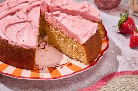 Brown Sugar Strawberry Frosted Cake seen from the side showing a thick layer of frosting and a golden cakey interior. - select to zoom