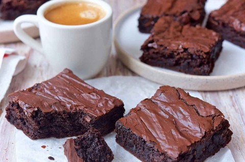 Several fudge brownies with shiny, crackly tops, sliced next to a cup of coffee - select to zoom