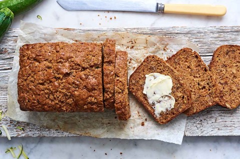An overhead photo of a loaf of zucchini bread. A few slices have been cut off the end, showing the tender interior crumb. One slice has softened butter spread on it. 