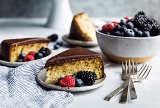 Two slices of yellow cake topped with fudge frosting on plates, garnished with fresh berries