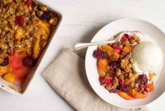 A pan of freshly baked, crumb-topped Summer Fruit Crisp next to a bowl of fruit crisp with a spoon