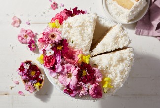A Old-Fashioned Coconut Cake coated in shredded coconut and decorated with a spray of edible flowers