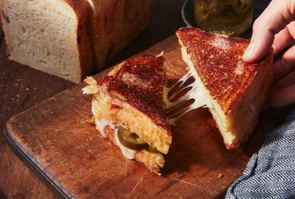 Hand pulling a triangle of a grilled cheese sandwich with cheese pull