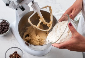 Hands adding flour to a stand mixer to make cookie dough