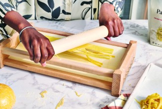 Pasta being pushed through a chitarra pasta cutter