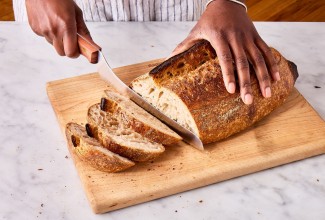 Hands slicing artisan bread loaf with an offset bread knife