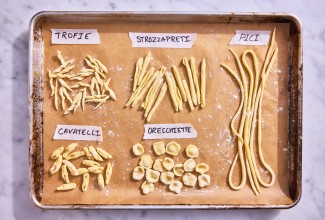 Different hand-shaped pasta types on a parchment-lined baking sheet