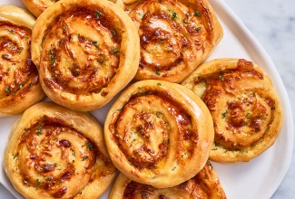 Overhead photograph of gluten free garlic parmesan swirl buns stacked on a light plate showing golden baked buns.