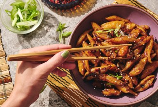 A person picking up hand cut noodles dressed with a dark umami sauce using chopsticks.