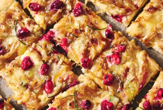 Sliced Caramelized Onion and Brie Pizza showing a golden baked top dotted with pomegranate, brie, and caramelized onion.