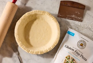 A rolling pin, pie crust, pastry knife, and bag of King Arthur Gluten-Free Pizza Flour shown on a counter and neatly arranged.