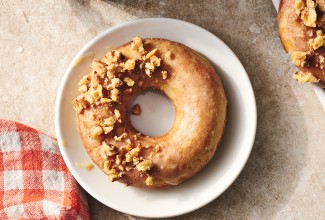 A Maple Donut on a plate with half coated in broke nut meat and the other half glazed.