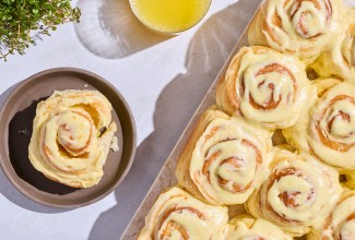 Fluffy Frosted Orange Rolls seen from above on a sheet tray with a single roll on a dark plate.