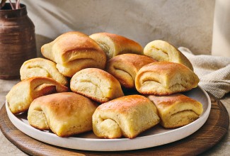 Parker house rolls stacked on a plate showing a buttery gloss and perfect folded bake.