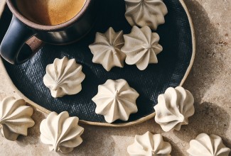 Espresso Meringues photographed from above and randomly spread on a dark plate with a cup of coffee in the upper left of the image.