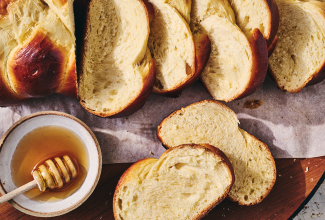 Challah bread sliced and shown on a counter with a bowl of honey next to the slices.