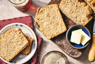 Sliced classic beer bread on a table with butter and a cutting board.