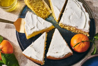 Sliced whole orange cake on a plate with white frosting and an orange.