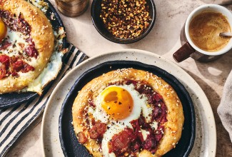 Breakfast Shakshuka shown on a plate with coffee and hot pepper flakes also in the picture.