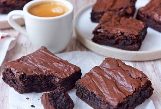 Several fudge brownies with shiny, crackly tops, sliced next to a cup of coffee