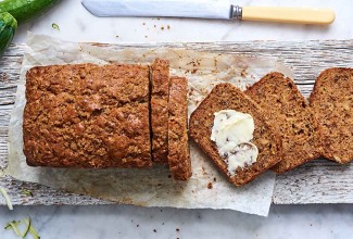 An overhead photo of a loaf of zucchini bread. A few slices have been cut off the end, showing the tender interior crumb. One slice has softened butter spread on it. 