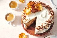 An overhead photo of a Hummingbird Cake with pineapple cream cheese frosting. A slice has been taken out of the cake and there are toasted nuts and a slice of dried pineapple on top of the cake. 