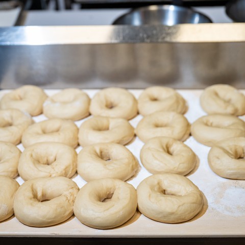 Photograph of twenty raw bagels on a sheet tray. - select to zoom