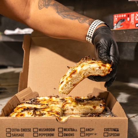 A photograph of a person lifting a slice of pizza out of a pizza box. - select to zoom