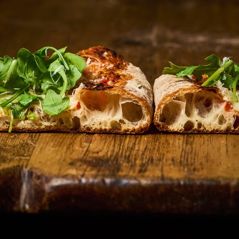 Two slices of artisanal pizza shown from the side with large air pockets in the cooked dough. - select to zoom