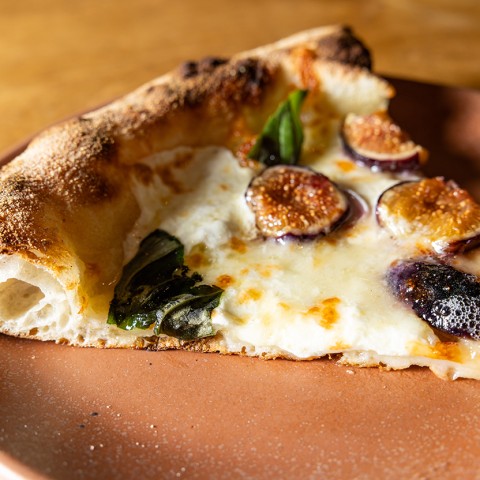A slice of cheesy pizza with dates and basil baked into the melted cheese. - select to zoom