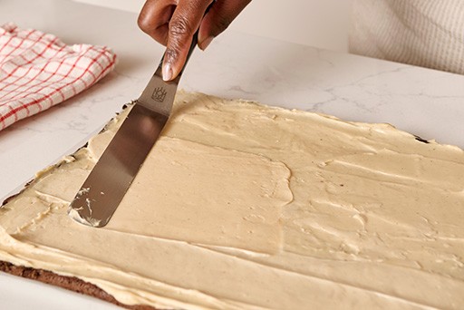 Spreading whipped cookie butter ganache on top of a chocolate sheet cake.