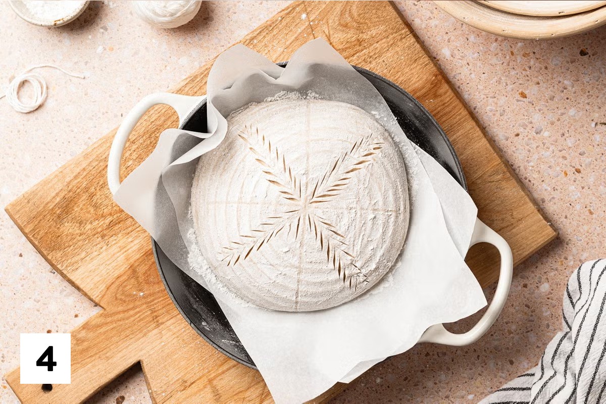 Loaf of sourdough bread dough with four wheat stalks scored to form an X