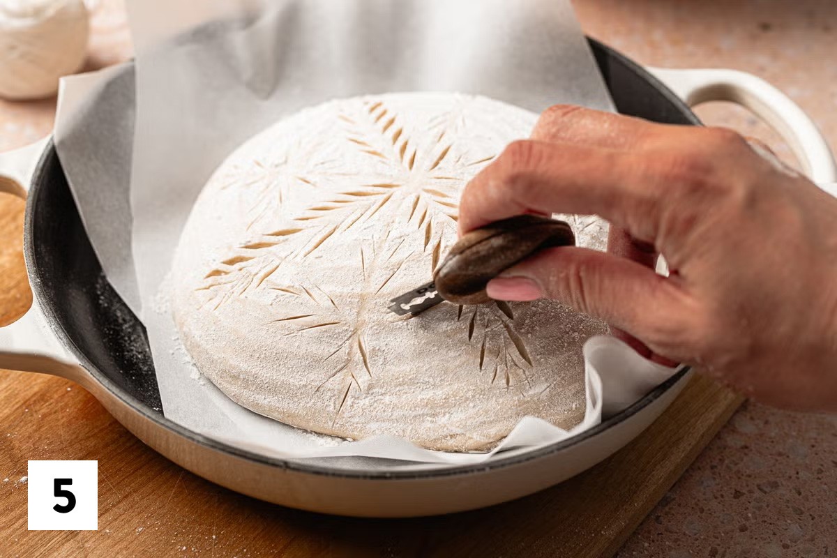 Scoring a wheat stalk pattern into a loaf of sourdough bread dough with a lame