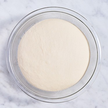 Pretzel bun dough in a clear glass bowl after rising to double size.