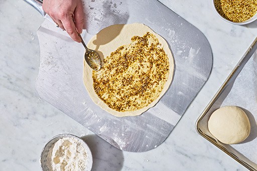 Adding topping to Zaatar Manakeesh dough before baking.