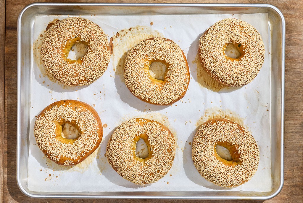 Sesame Sourdough Discard Bagels freshly out of the oven and still on their parchment paper and baking sheet.