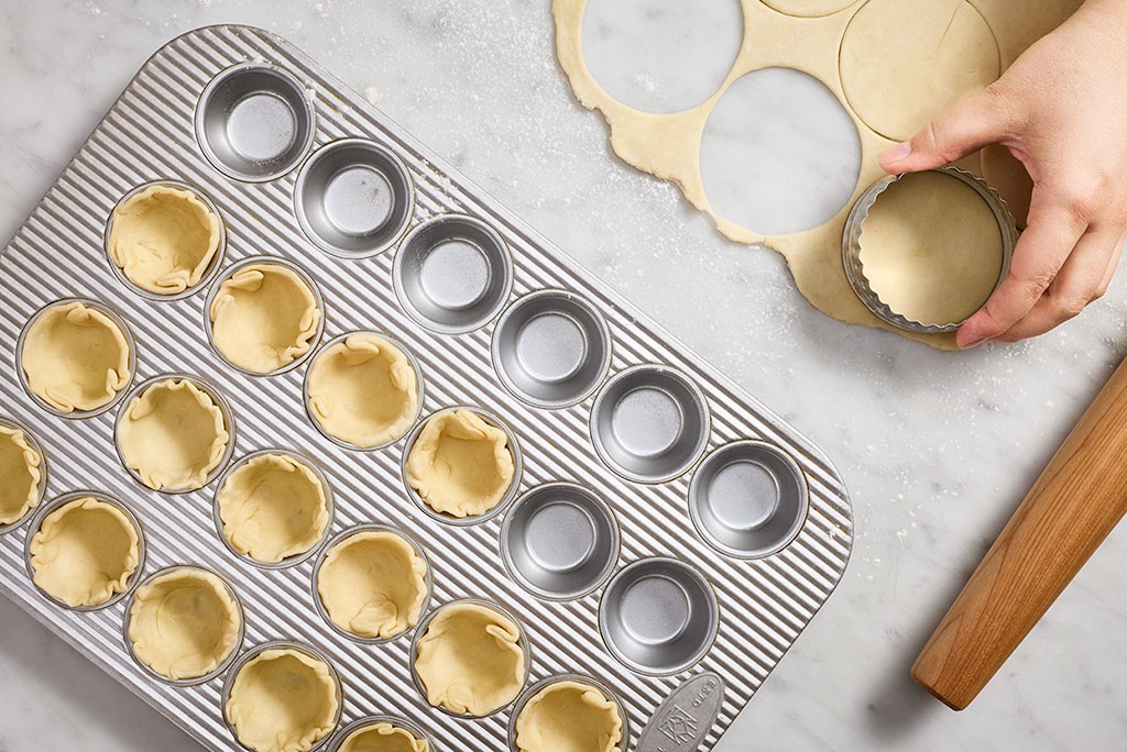 Preparing cups of dough in a mini muffin pan for Mini Quiches