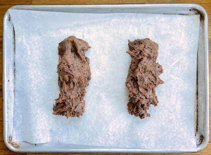 Two logs of biscotti dough on a parchment-lined baking sheet, showing generous spacing between them.
