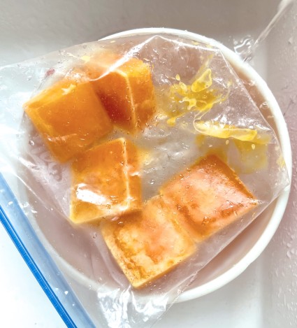 Frozen eggs in a zip-top bag thawing in a bowl set under a stream of trickling water.