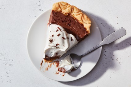 A slice of Chocolate Cream Pie on a plate, topped with whipped cream and chocolate shavings, with a bite on a fork