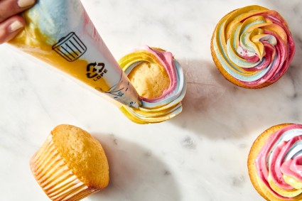 Piping rainbow frosting onto cupcakes